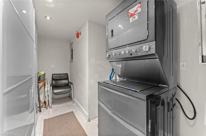 Clothes washing area featuring light tile patterned floors, stacked washer and dryer, baseboards, and laundry area