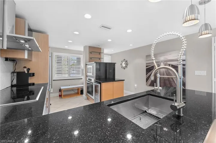 Kitchen with black electric cooktop, light tile patterned floors, dark stone counters, a sink, and visible vents