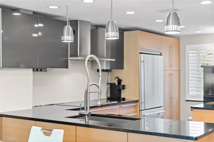 Kitchen featuring refrigerator, modern cabinets, dark stone countertops, light brown cabinets, and decorative light fixtures