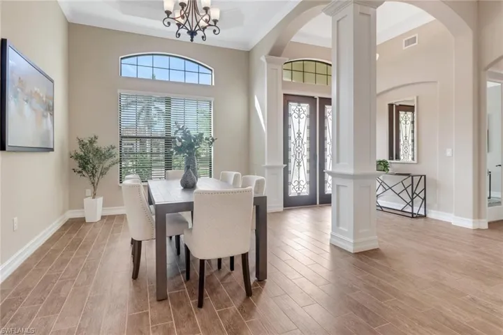 Dining room with ornate columns, an inviting chandelier, arched walkways, and light wood-style floors