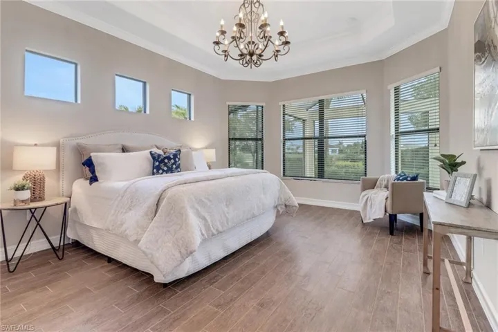 Primary bedroom  with an ensuite bathroom, wood finished floors, ornamental molding, and a raised ceiling.