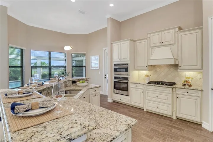 Kitchen with custom exhaust hood, tasteful backsplash, double oven, wood tiled floor, and a sink