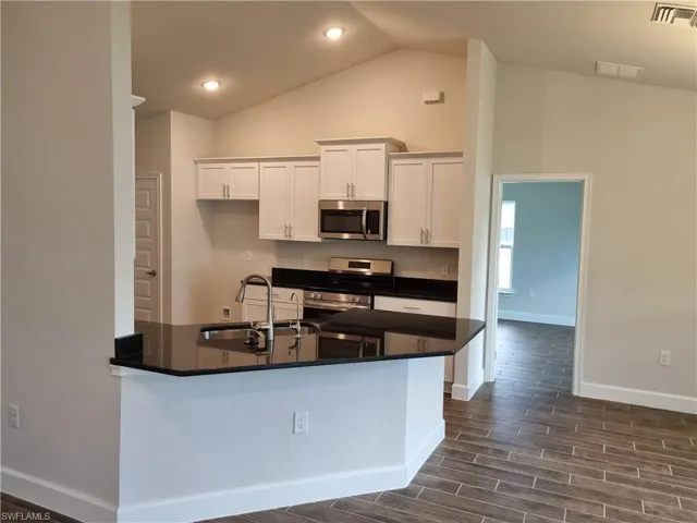 Kitchen with white cabinetry, stainless steel appliances, sink, dark hardwood / wood-style floors, and vaulted ceiling