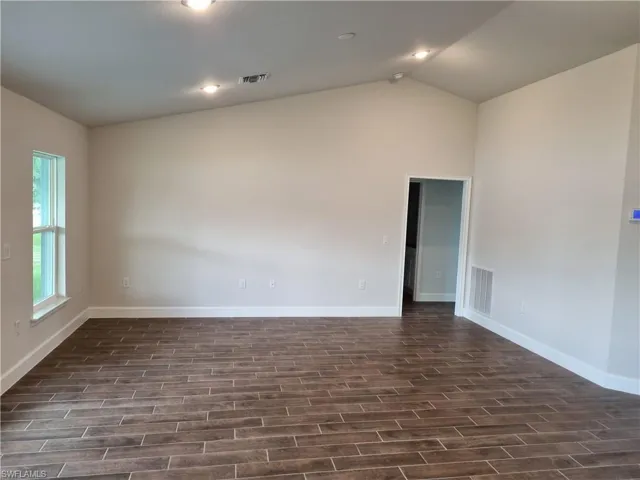 Empty room featuring dark wood-type flooring and vaulted ceiling