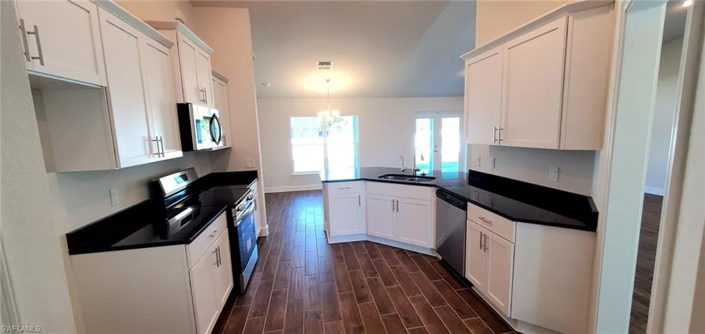 Kitchen featuring white cabinets, appliances with stainless steel finishes, dark hardwood / wood-style floors, and a chandelier