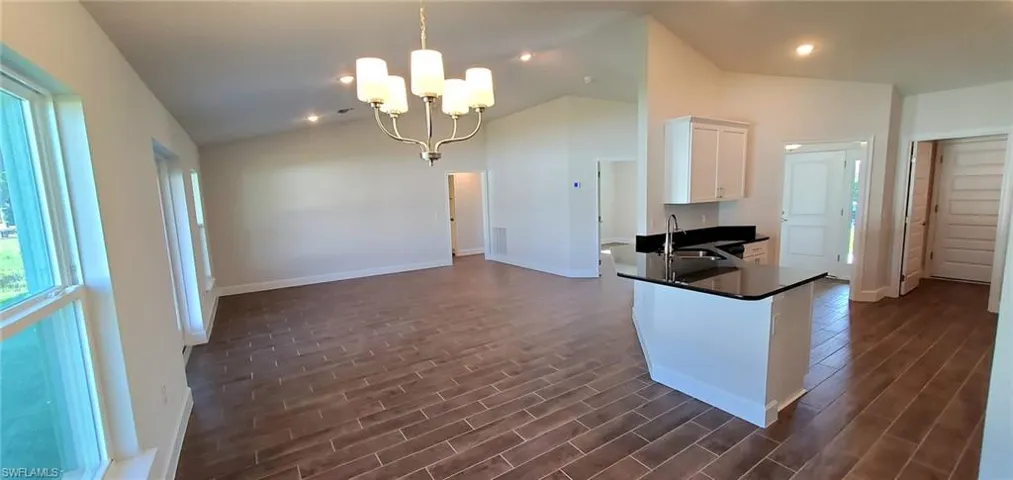 Kitchen featuring dark wood-style tile floors, a notable chandelier, kitchen peninsula, lofted ceiling, and white cabinets