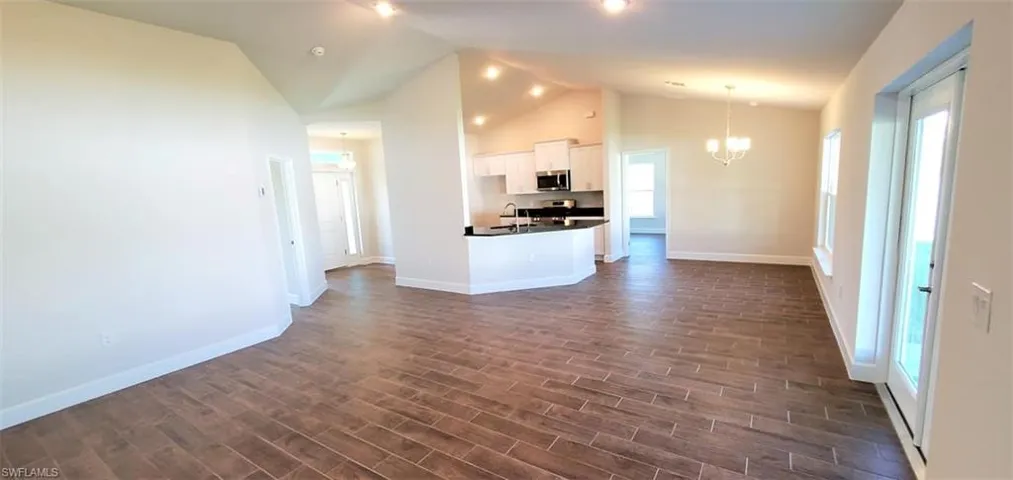 Kitchen with hanging light fixtures, a notable chandelier, white cabinetry, dark wood-type flooring, and a center island with sink