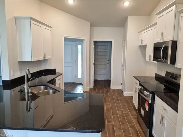 Kitchen with dark hardwood / wood-style flooring, appliances with stainless steel finishes, sink, white cabinetry, and dark stone countertops