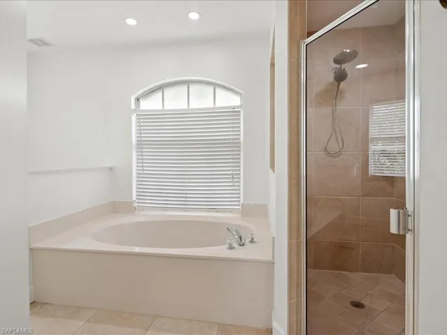 Soaking tub with a large arched window, complemented by a glass-enclosed shower featuring a handheld shower head and tiled surround