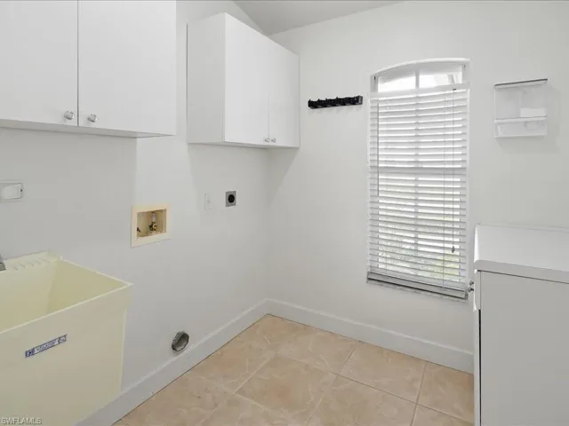 Utility room featuring neutral tile flooring, white cabinetry, a utility sink, and a window with blinds