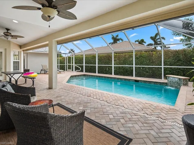 Screened lanai featuring a swimming pool with a stone waterfall feature, paver deck, and two ceiling fans