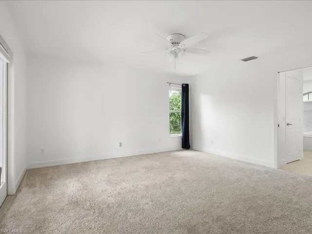 Spacious room featuring neutral carpeting, a ceiling fan with integrated lighting, a large window, a light-filled doorway, and a white interior door