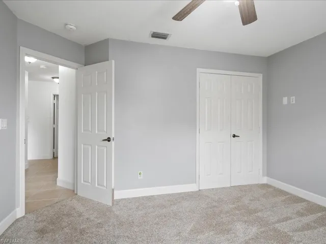Carpeted room with a ceiling fan, light gray wall paint, white baseboards, and white six-panel bifold closet doors
