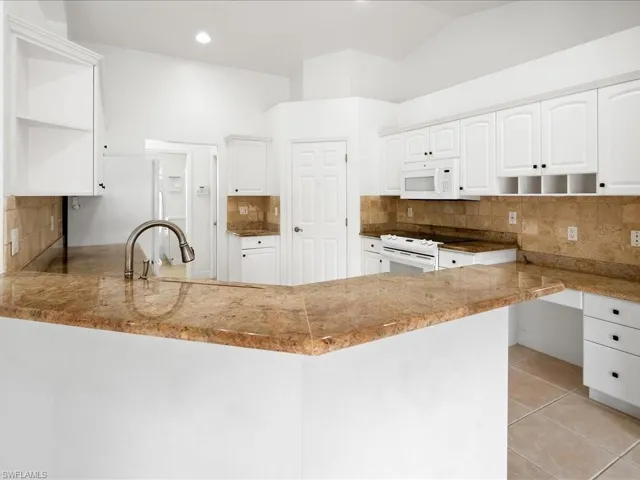 Kitchen featuring white cabinetry, light-toned granite countertops, a stainless steel pull-down faucet, a tile backsplash, and a white oven with an overhead microwave