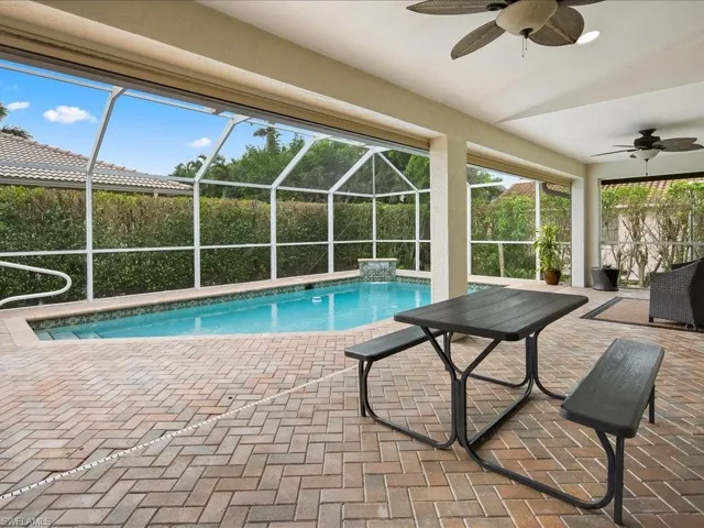 Screened-in pool deck featuring a swimming pool with a waterfall feature, a spacious covered patio, herringbone-patterned brick pavers, and ceiling fans
