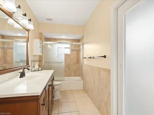 Bathroom featuring a dark wood finish vanity with integrated sink, a large wall mirror, and a shower-tub combination with sliding glass doors