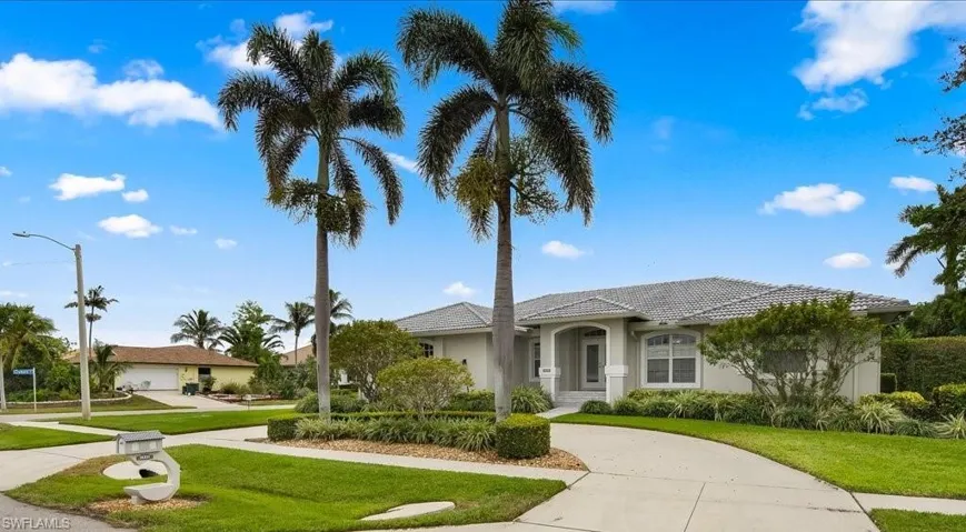 A curved concrete driveway leads to a single-story residence featuring a light gray exterior, a gray tile roof, and an arched entry