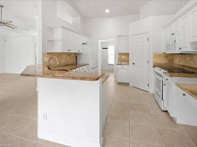 Open-concept kitchen featuring white cabinetry, granite-finish countertops, and a tile backsplash