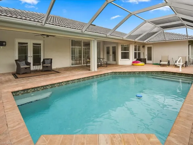 Screened pool enclosure featuring a rectangular pool with integrated steps, brick coping, and a tiled waterline