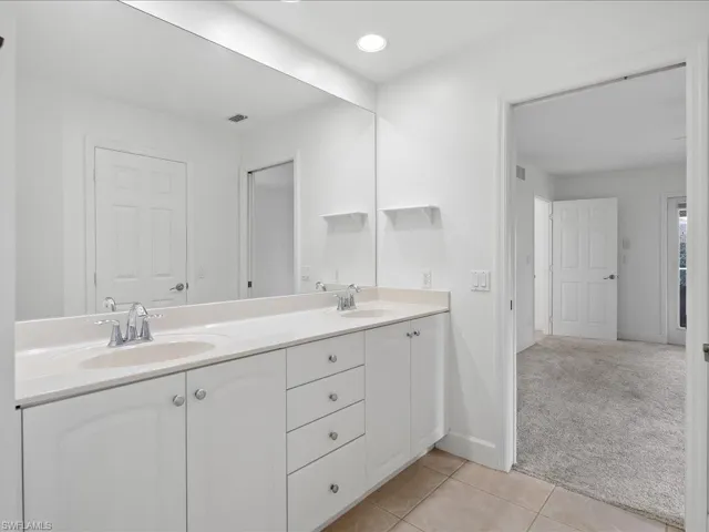 Dual sink vanity with white cabinetry and chrome fixtures, illuminated by a recessed ceiling light