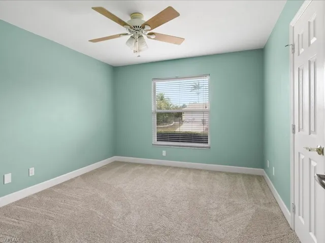 Spacious room featuring neutral carpeting, light teal walls, and white baseboards