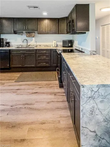 Kitchen with black appliances, light wood-style flooring, and dark brown cabinets