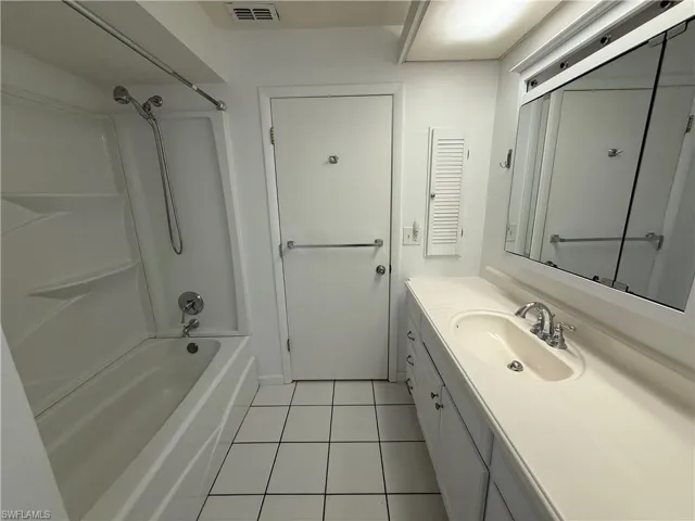 Bathroom featuring a shower/tub combination, a single vanity with an integrated sink, a mirrored medicine cabinet, square tile flooring, and a louvered wall cabinet