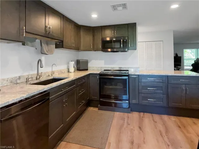 Kitchen with appliances with stainless steel finishes, light wood-style flooring, light stone counters, and recessed lighting