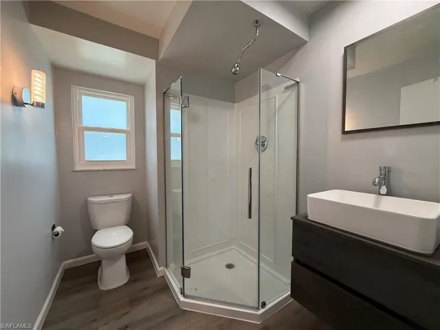 Full bathroom featuring a rectangular vessel sink, dark wood-finish vanity, glass-enclosed corner shower, and wood-finish flooring