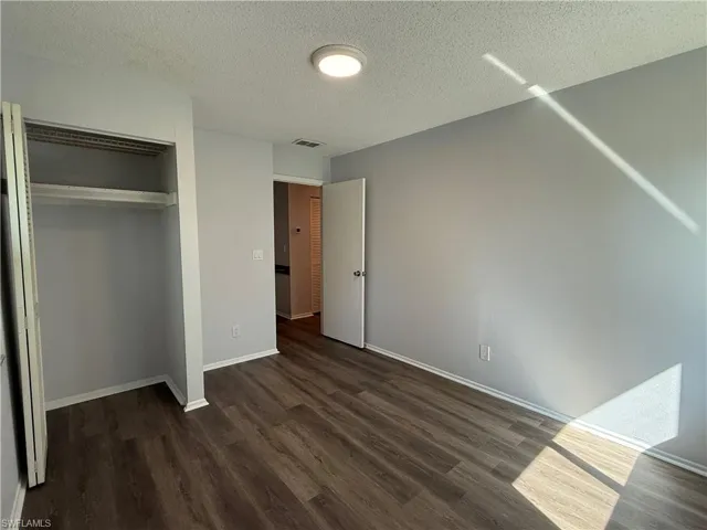Room featuring wood-finish flooring, light grey walls, white trim, and an open closet with shelving and bi-fold doors