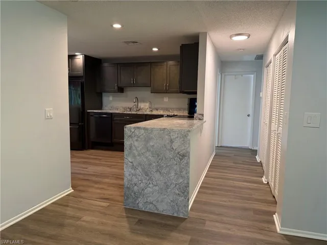 Kitchen and hallway area featuring wood-finish flooring, dark wood cabinetry, light-toned countertops, and a kitchen peninsula with a matching countertop