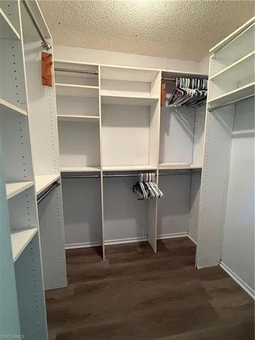 Custom-designed closet system featuring white shelving, multiple hanging rods, and wood-finish flooring