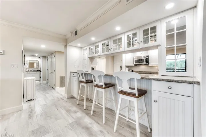 Kitchen with white cabinets, glass insert cabinets, a breakfast bar, ornamental molding, and stainless steel microwave