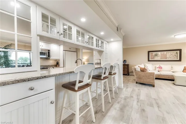 Kitchen featuring white cabinetry, ornamental molding, light stone countertops, a breakfast bar, and glass insert cabinets