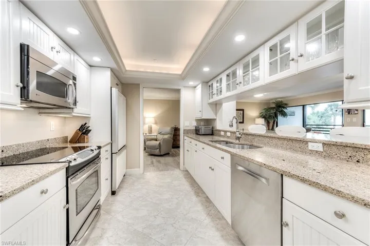Kitchen featuring appliances with stainless steel finishes, glass insert cabinets, ornamental molding, light stone counters, and recessed lighting