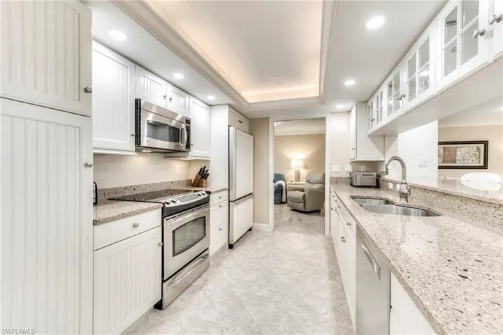 Kitchen with stainless steel appliances, light stone countertops, white cabinetry, glass insert cabinets, and recessed lighting