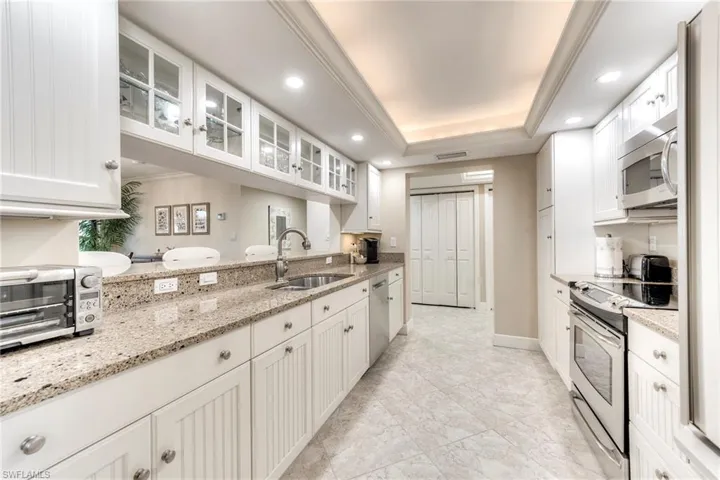 Kitchen with glass insert cabinets, ornamental molding, appliances with stainless steel finishes, light stone counters, and white cabinets