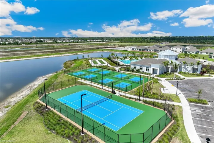 Aerial view showcasing recreational amenities, including a tennis court, multiple pickleball courts, and a community building with a swimming pool