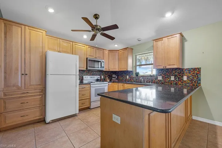 Kitchen with white appliances, light tile patterned floors, backsplash, ceiling fan, and kitchen peninsula
