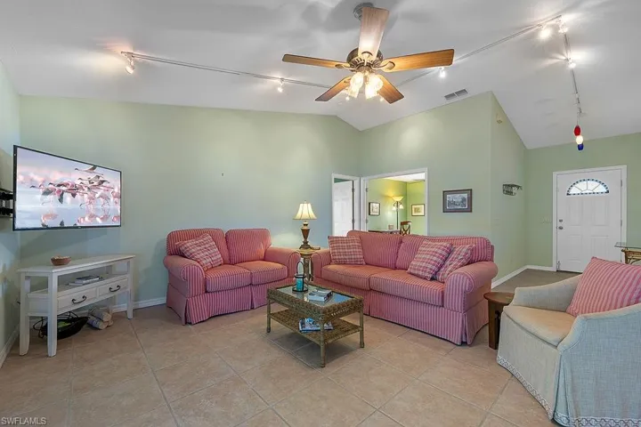 Living room featuring ceiling fan, vaulted ceiling, track lighting, and light tile patterned flooring
