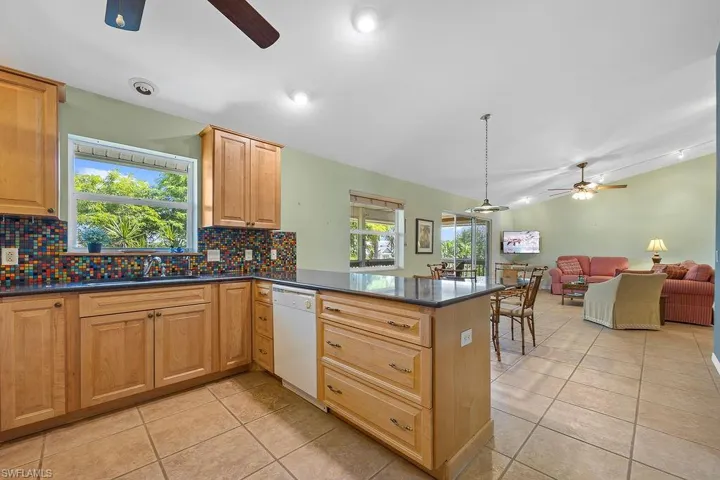 Kitchen with ceiling fan, white dishwasher, kitchen peninsula, and decorative backsplash