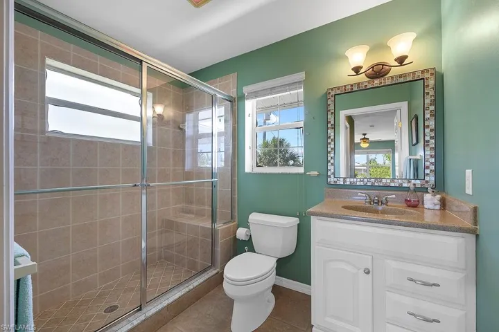 Bathroom with a shower with shower door, vanity, tile patterned flooring, and toilet