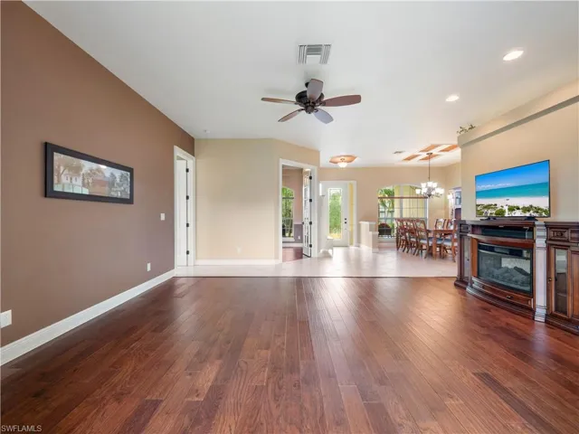 Living room with ceiling fan with notable chandelier and dark wood-type flooring