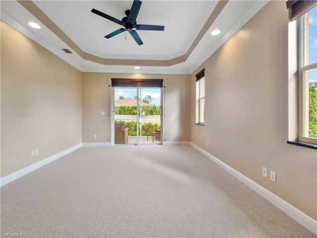 Carpeted empty room featuring a raised ceiling, ceiling fan, and ornamental molding