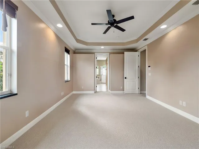 Carpeted empty room featuring plenty of natural light, ceiling fan, ornamental molding, and a tray ceiling