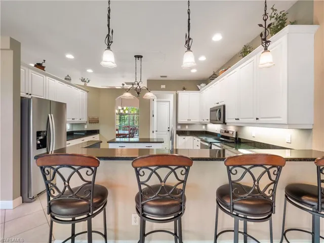 Kitchen with white cabinets, stainless steel appliances, hanging light fixtures, and a breakfast bar area