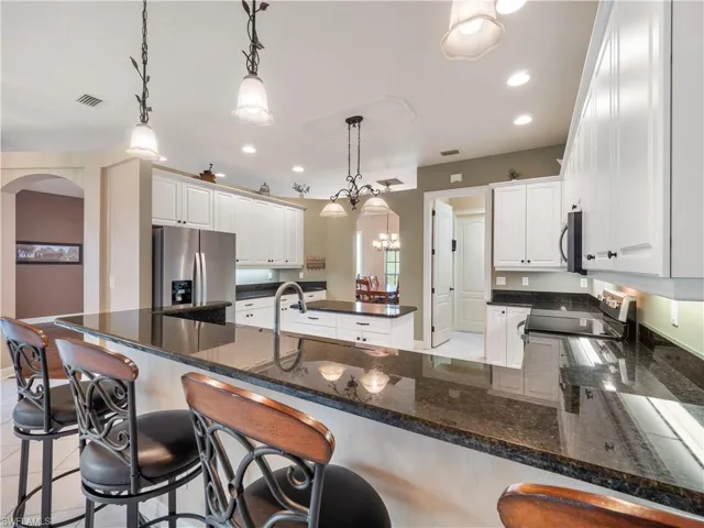 Kitchen with white cabinets, appliances with stainless steel finishes, and decorative light fixtures