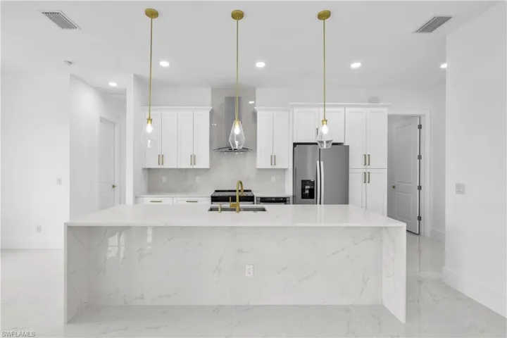 Kitchen with backsplash, a center island with sink, pendant lighting, wall chimney range hood, and stainless steel fridge with ice dispenser