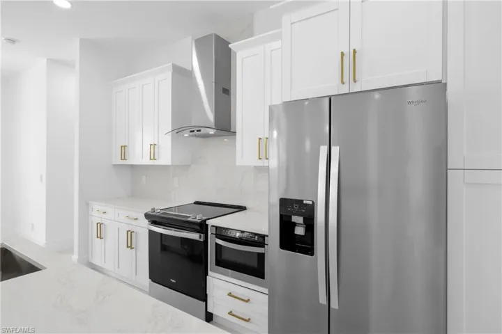 Kitchen with decorative backsplash, light stone counters, stainless steel appliances, wall chimney range hood, and white cabinets