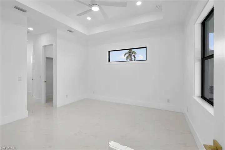 Tiled empty room with ceiling fan and a tray ceiling